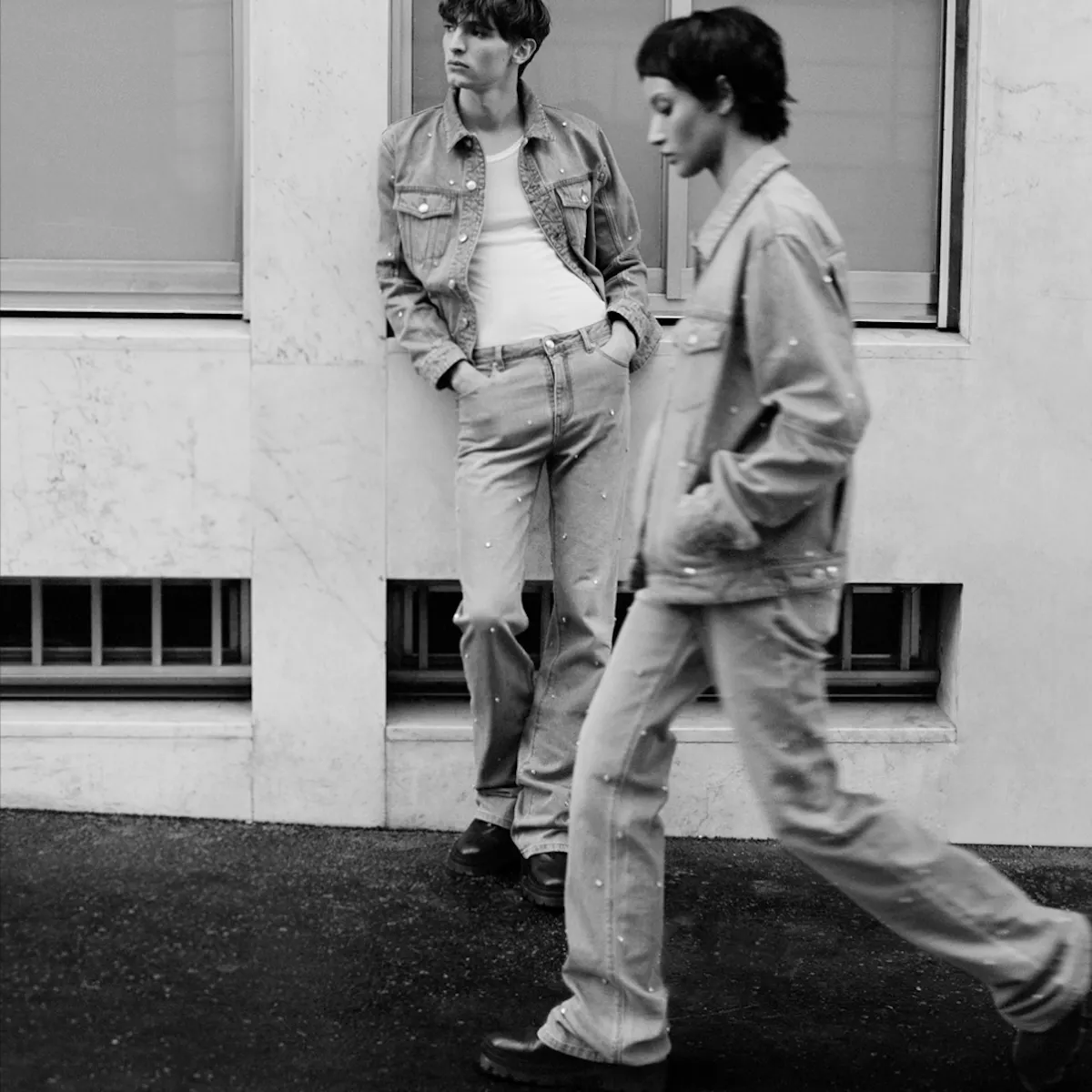 Due silhouette in jeans camminano lungo un muro di strada, fotografia in bianco e nero.