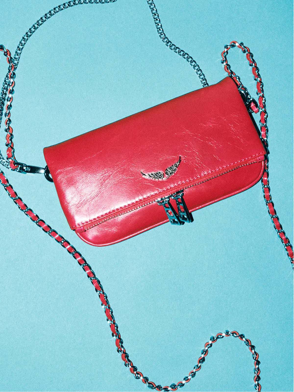Mini Rock clutch in red leather with silver wings and interwoven chain, on a turquoise background.