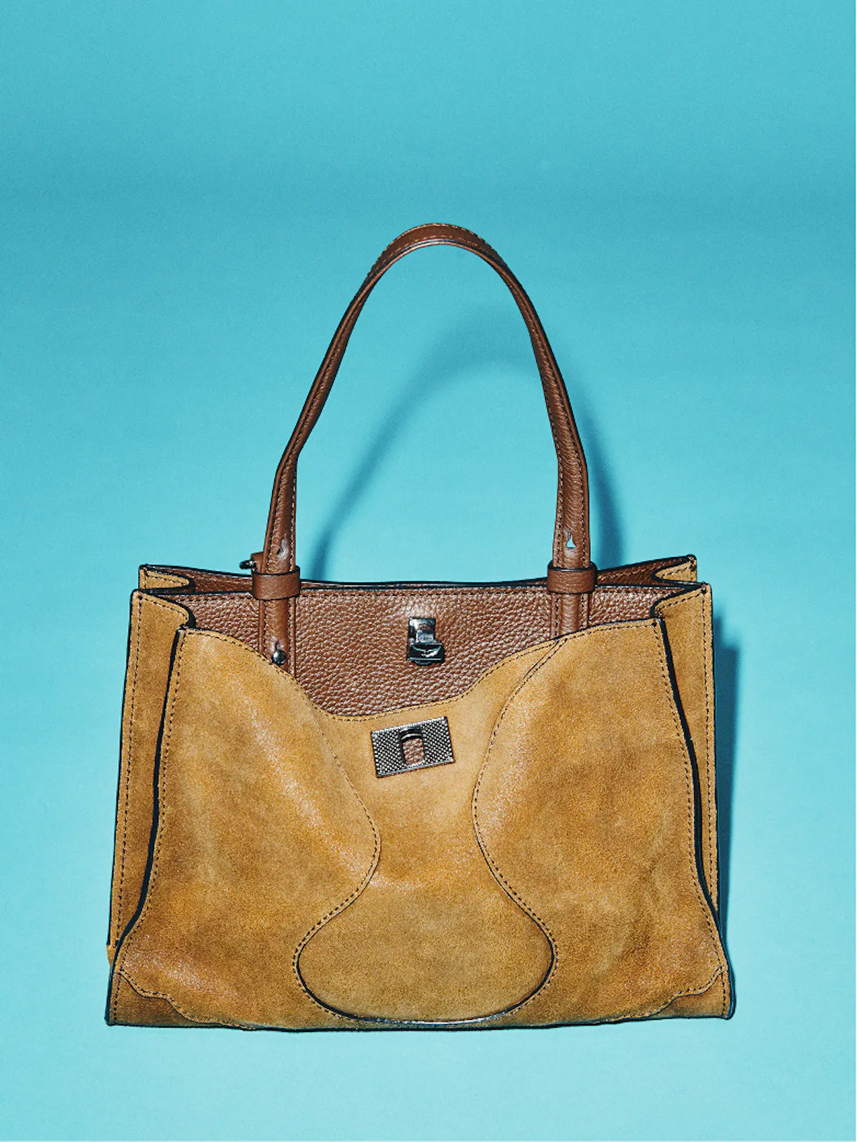 Camel suede handbag with a croc-effect flap and brown leather handles, on a turquoise background.