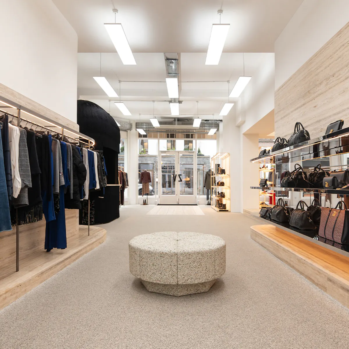 Central aisle of the King’s Road boutique: a stone pouf, clothing rails on the left, a wall of bags on the right and the black bearskin-shaped till at the back.