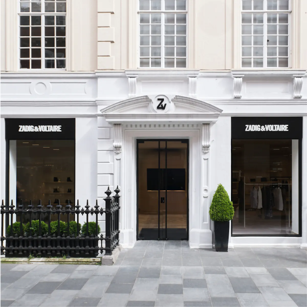 Façade blanche d’une boutique Zadig&Voltaire à deux vitrines, enseignes noires et porte noire sous un fronton